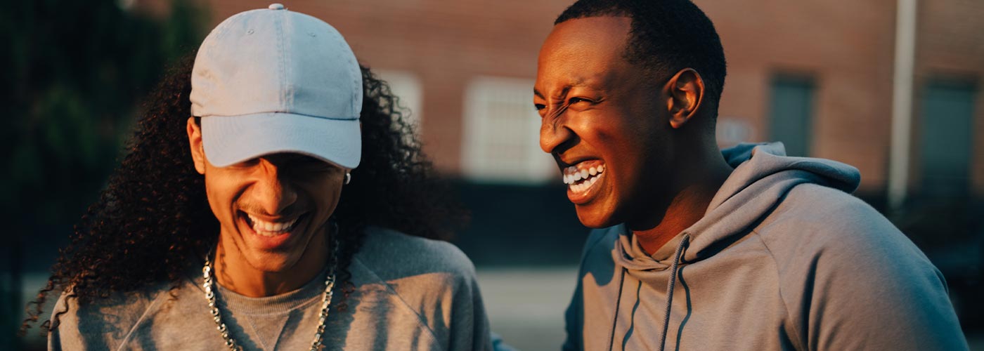 Two young men smiling and laughing together, enjoying a joyful moment in a casual setting.