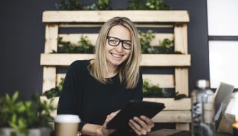 A smiling professional woman holds a tablet in a modern workspace, representing top productivity apps for working students