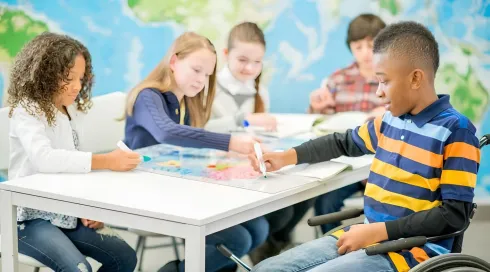 A diverse group of children and a teacher engage in inclusive early childhood education activities in a classroom.
