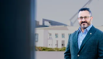 1. A man wearing glasses and a suit stands confidently in front of a modern building.