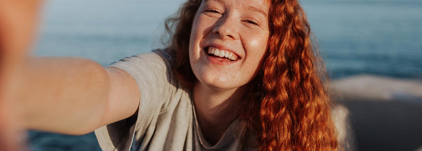 A woman with red hair smiles warmly at the camera, exuding a cheerful and friendly demeanor.