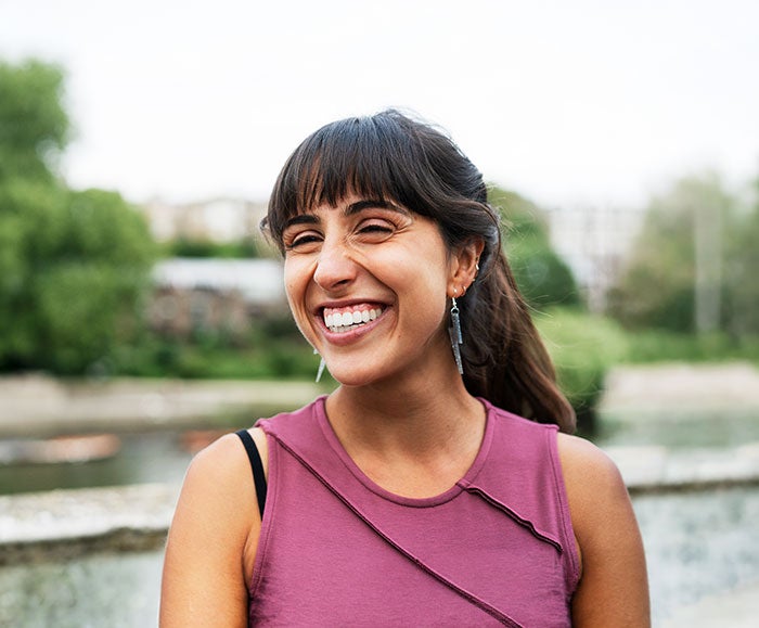 1. A woman smiles joyfully while standing in front of a flowing river, surrounded by lush greenery.