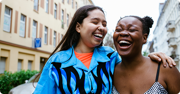 1. Two women share a joyful moment, laughing together on a lively street.